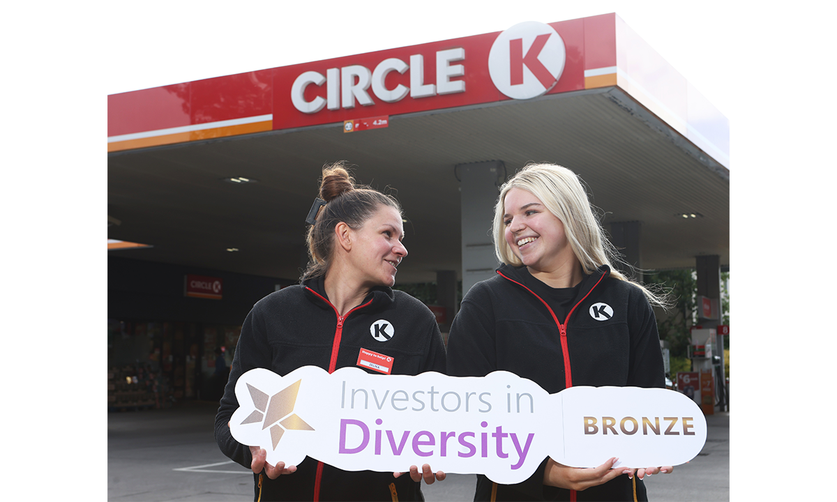 Two Circle K staff members stand smiling outside a Circle K station, holding a sign that reads 'Investors in Diversity Bronze'